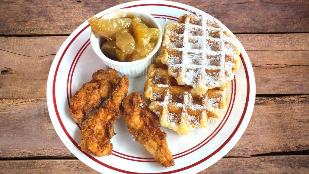 Chicken tenders with waffles and fruit compote on a white plate with red rim