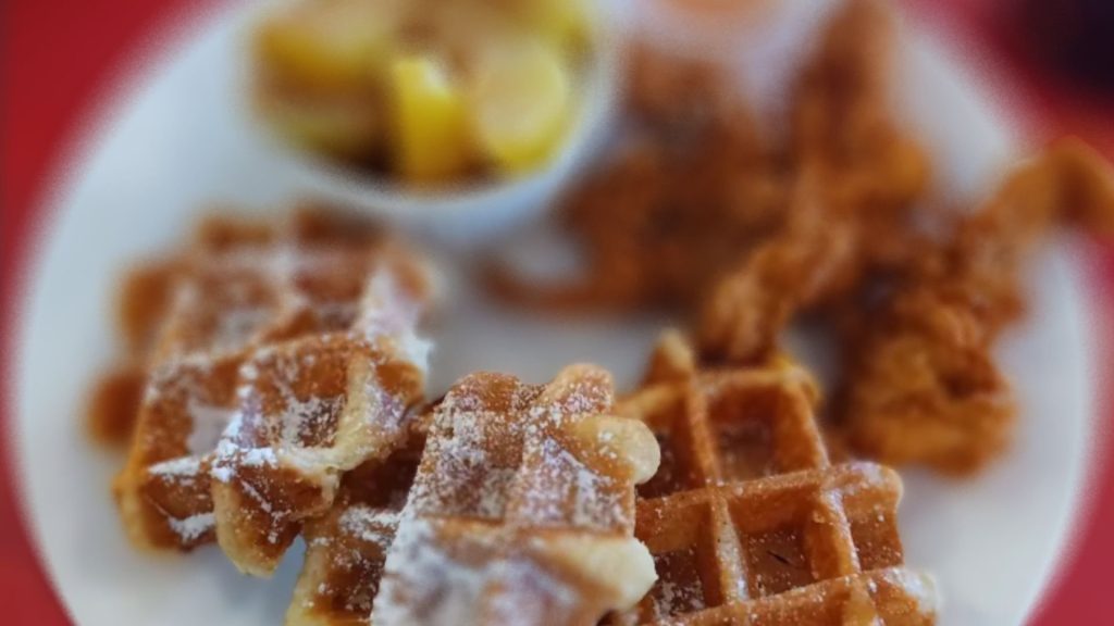 Close-up of waffles dusted with powdered sugar and served with fried chicken